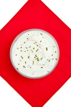 Close up of a bowl of white dip with herbs on a red napkin against a white background