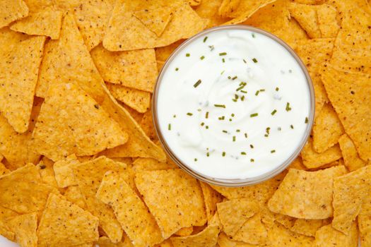 Bowl of white dip with herbs surrounded by nachos