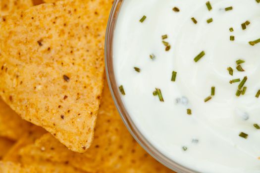 Close up of a bowl of white dip with herbs  beside nachos
