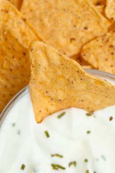 Close up of a bowl of white dip with herbs and a nacho dipped in it