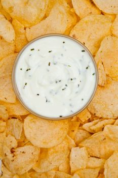 Close up of a bowl of white dip with herbs surrounded by nachos