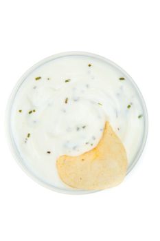 Close up of a bowl of white dip with herbs and a chips dipped in it against a white background
