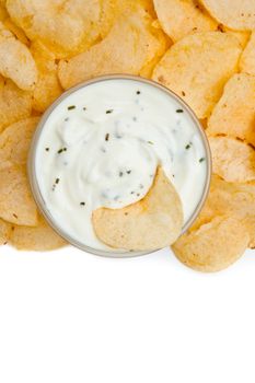 Close up of a bowl of dip with herbs ans a nacho dipped in it against a white background