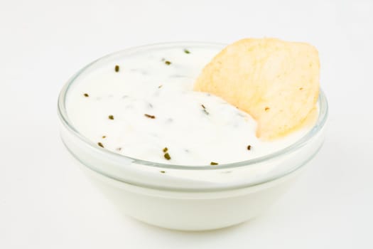 Bowl of white dip with herbs and a nacho dipped in it against a white background