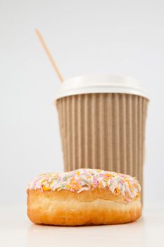 A multi coloured doughnut and a cup of tea placed together against a white background