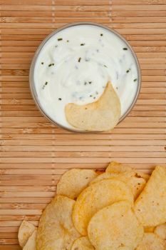Close up of a bowl of white dip with herbs beside chips
