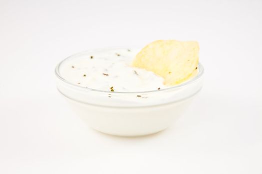 Bowl of dip with herbs with a chip dipped in it against a white background