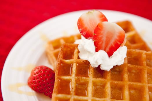 Half cut strawberry and whipped cream on a white plate on a red napkin