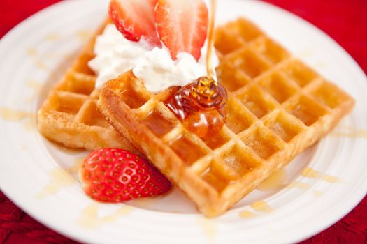 Waffles with whipped cream and strawberries and syrup on a white plate