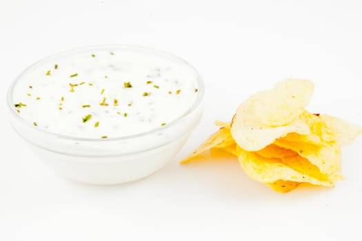 Bowl of a white dip with herbs and chips against white background