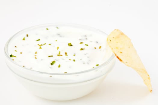 Bowl of white dip with herbs and a chips against a white background