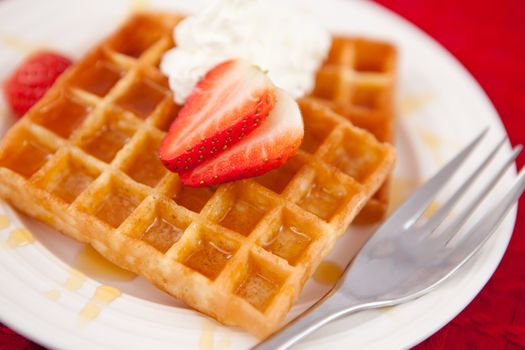 Waffles with whipped cream and strawberry on it on a red napkin