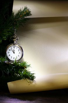 New Year decoration. Vintage pocket watch hanging near firtree against blank scroll