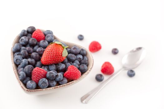 Berries in  a heart shaped bowl  with spoon against a white background