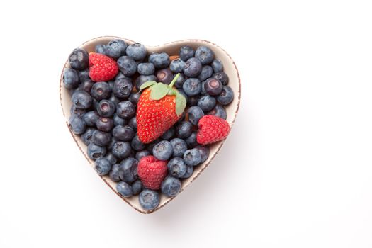Different berries in  a heart shaped bowl against a white background