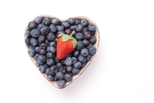 Blueberries and one Strawberry  in  a heart shaped bowl against a white background
