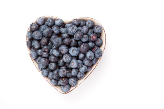 Blueberries in a heart shaped bowl against a white background
