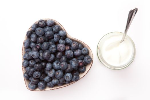 White yogurt and blueberries in a heart shaped bowl   against a white background