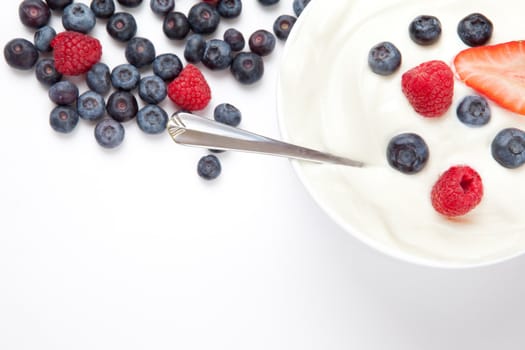 Bowl of cream with berries and a spoon against a white background