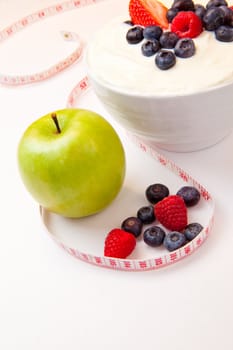 Apple and bowl of berries cream and  a tape measure against a white background