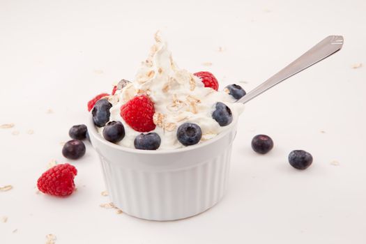 White jar of berries and whipped cream with spoon  against white background