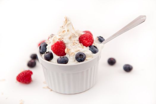 Jar of blueberries and raspberries in a whipped cream against white background