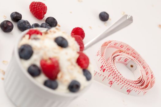 Tape measure and a dessert of berries against a white background