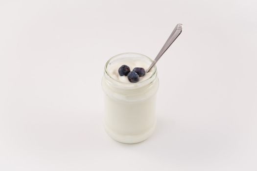 Pot of yoghurt with three blueberries against a white background