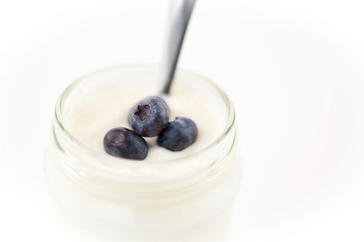 Close up of a pot of yoghurt with blueberries against a white background