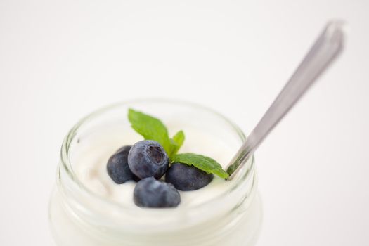Close up of a pot of yoghurt with blueberries and fresh mint against a white background