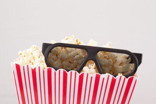 3D glasses on top of a box of popcorn against white background