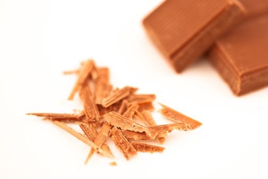 Blurred chocolate pieces and chocolate shaving against a white background