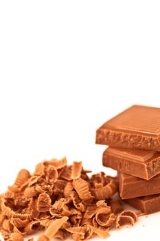 Four pieces of chocolate piled beside chocolate shavings against a white background