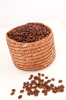 Close up of a basket full of coffee seeds with seeds lying in front of it against a white background