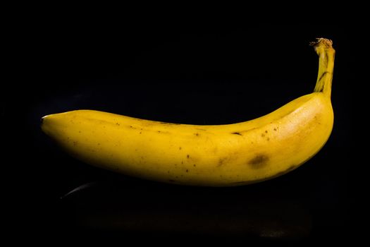 One fresh, yellow banana on black background with reflection