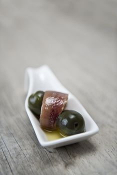 Anchovy appetizer served with green olives in a china spoon.