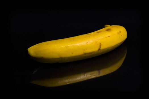 One fresh, yellow banana on black background with reflection