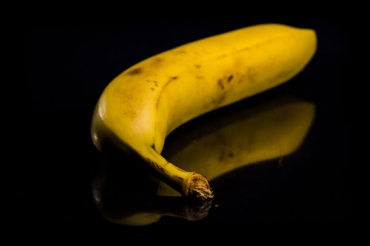 One fresh, yellow banana on black background with reflection