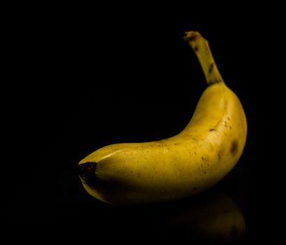 One fresh, yellow banana on black background with reflection