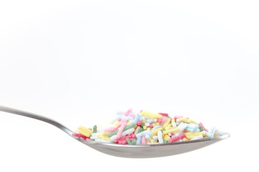 Multicolored sprinkles on the spoon on a white background