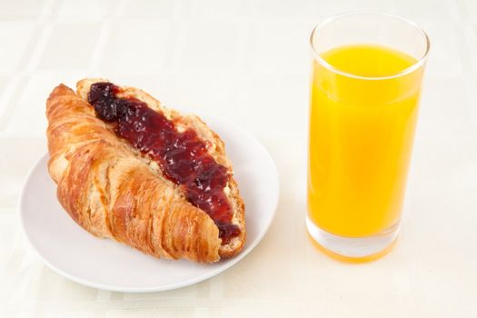 Croissant next to a glass of orange juice against white background