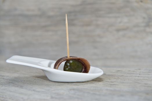 Anchovy appetizer served with green olives in a china spoon on a wooden background