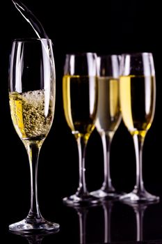 Full glasses of champagne and one being filled against black background