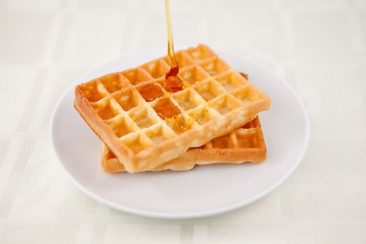 Honey falling on a waffle on a table