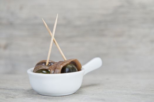 Anchovy appetizer served with green olives in a china spoon on a wooden background