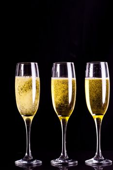 Three full glasses of champagne against black background