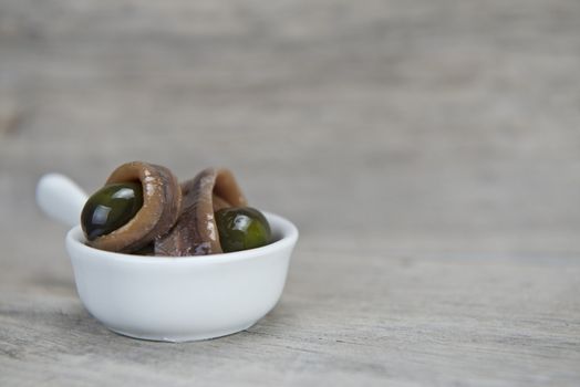 Anchovy appetizer served with green olives in a china spoon on a wooden background