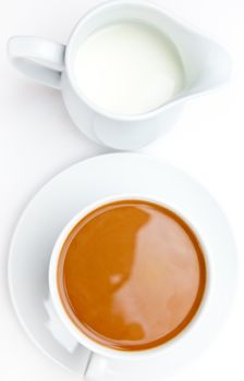 White cup of coffee next to a milk pot against white background