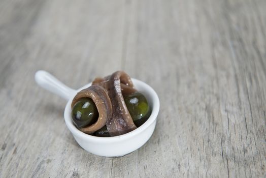 Anchovy appetizer served with green olives in a china spoon on a wooden background