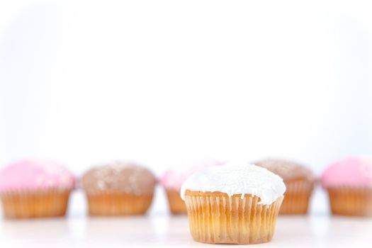 White muffin placed in front of a line of muffin with icing sugar against a blue background